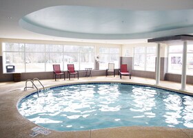 Una piscina interior con agua cristalina, rodeada de ventanas y sillas rojas.