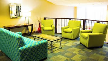 A hotel lobby with a blue patterned sofa, a glass coffee table, and three green armchairs.