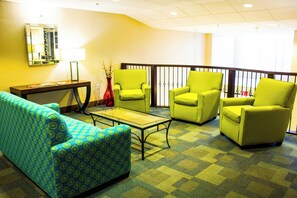 Un hall de hotel con un sofá estampado azul, una mesa de centro de vidrio y tres sillones verdes.