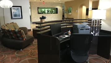 A hotel room with a desk, office chair, sofa, and a decorative wall with a plant.