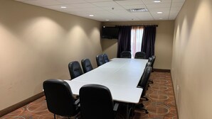 A conference room with a long table, black chairs, a flat-screen TV, and patterned carpet.