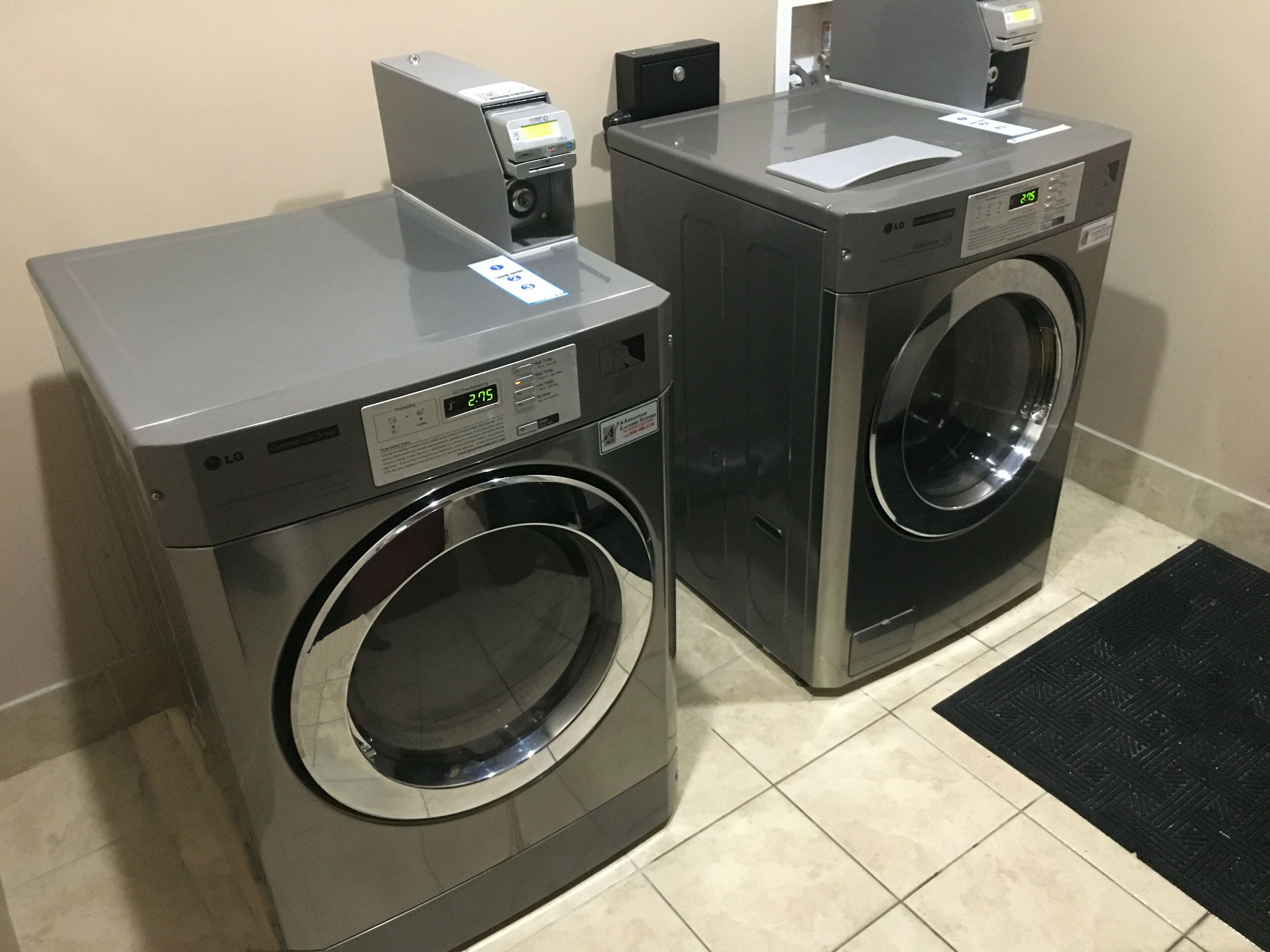 Dos lavadoras de carga frontal con pantallas digitales, un panel de control y un pequeño dispensador de papel.