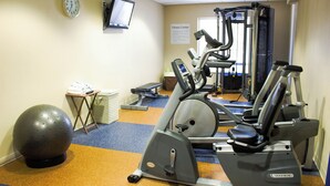 A fitness center with exercise equipment, a ball, and a television on the wall.