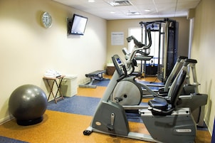 Un gimnasio con equipo de ejercicio, una pelota y un televisor en la pared.