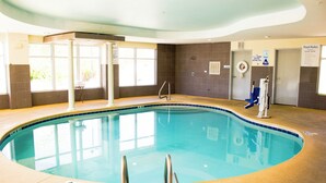 An indoor swimming pool with clear water, a lifebuoy, and a pool rule sign.