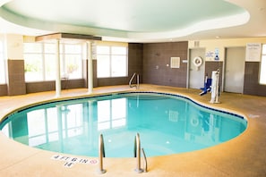 An indoor swimming pool with clear water, a lifebuoy, and a pool rule sign.
