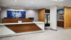A reception area with a wooden reception desk, a blue wall with geometric patterns, and a refrigerator stocked with beverages.
