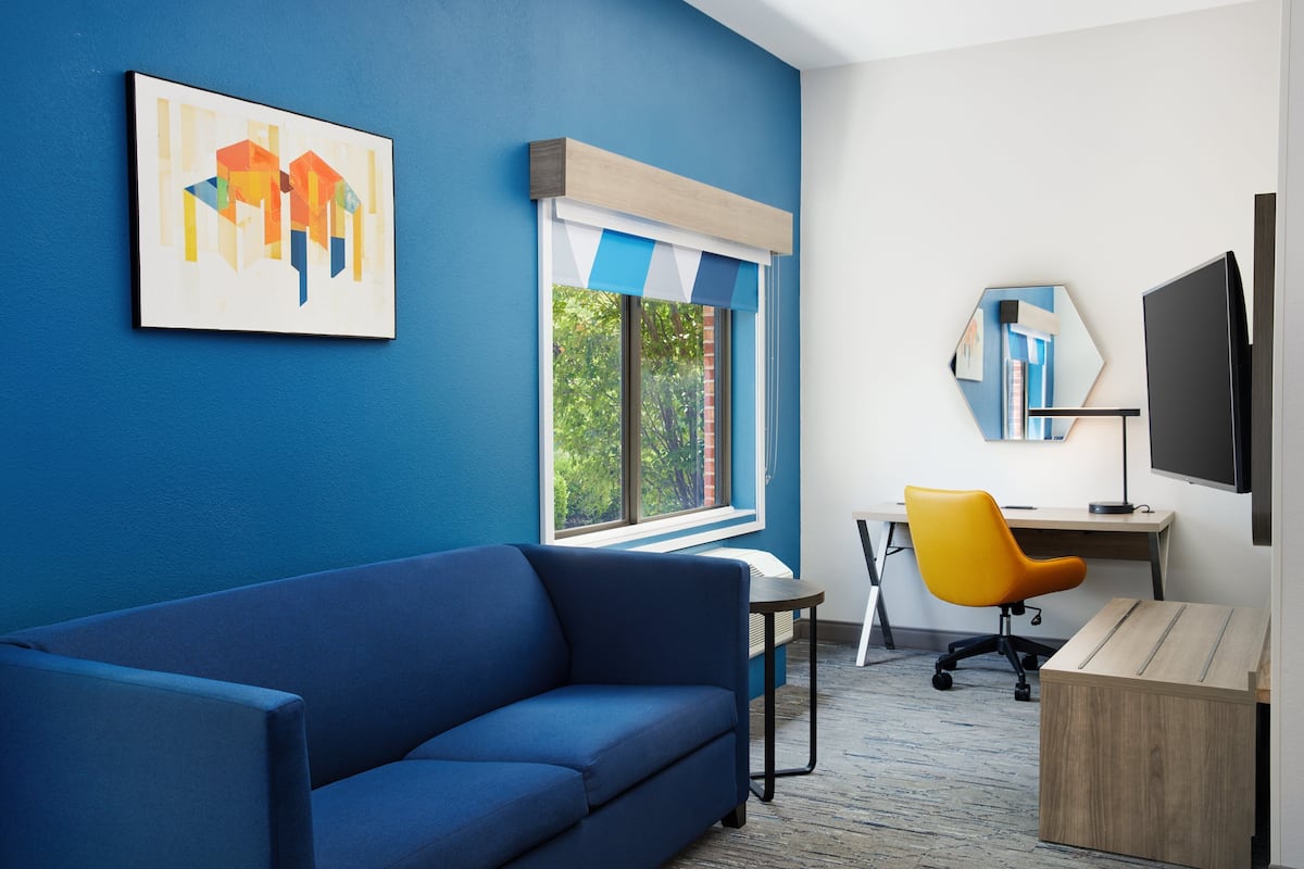 Une pièce moderne avec un canapé bleu, un bureau avec un ordinateur, une chaise de bureau jaune et un grand miroir.