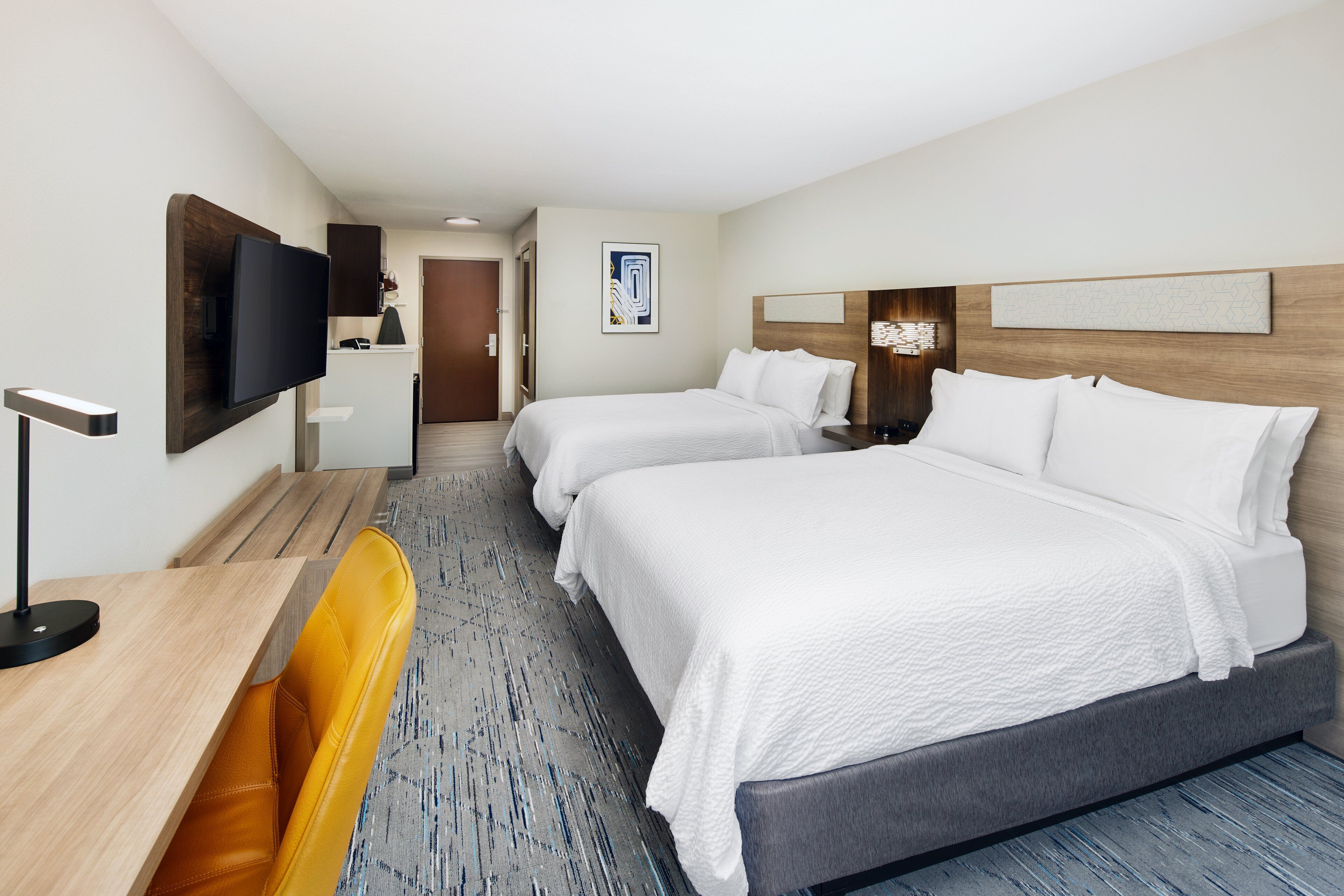 A hotel room with two beds, a desk, a chair, a TV, and a door leading to a bathroom.