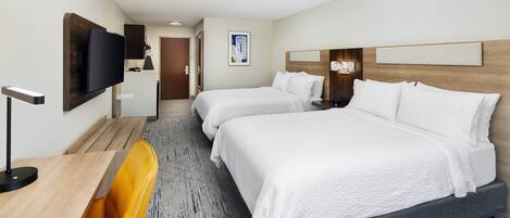 A hotel room with two beds, a desk, a chair, a TV, and a door leading to a bathroom.