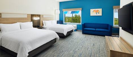 A hotel room with two beds, a blue sofa, a TV, and a window with a view.