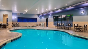 An indoor swimming pool with clear water, surrounded by lounge chairs and tables.