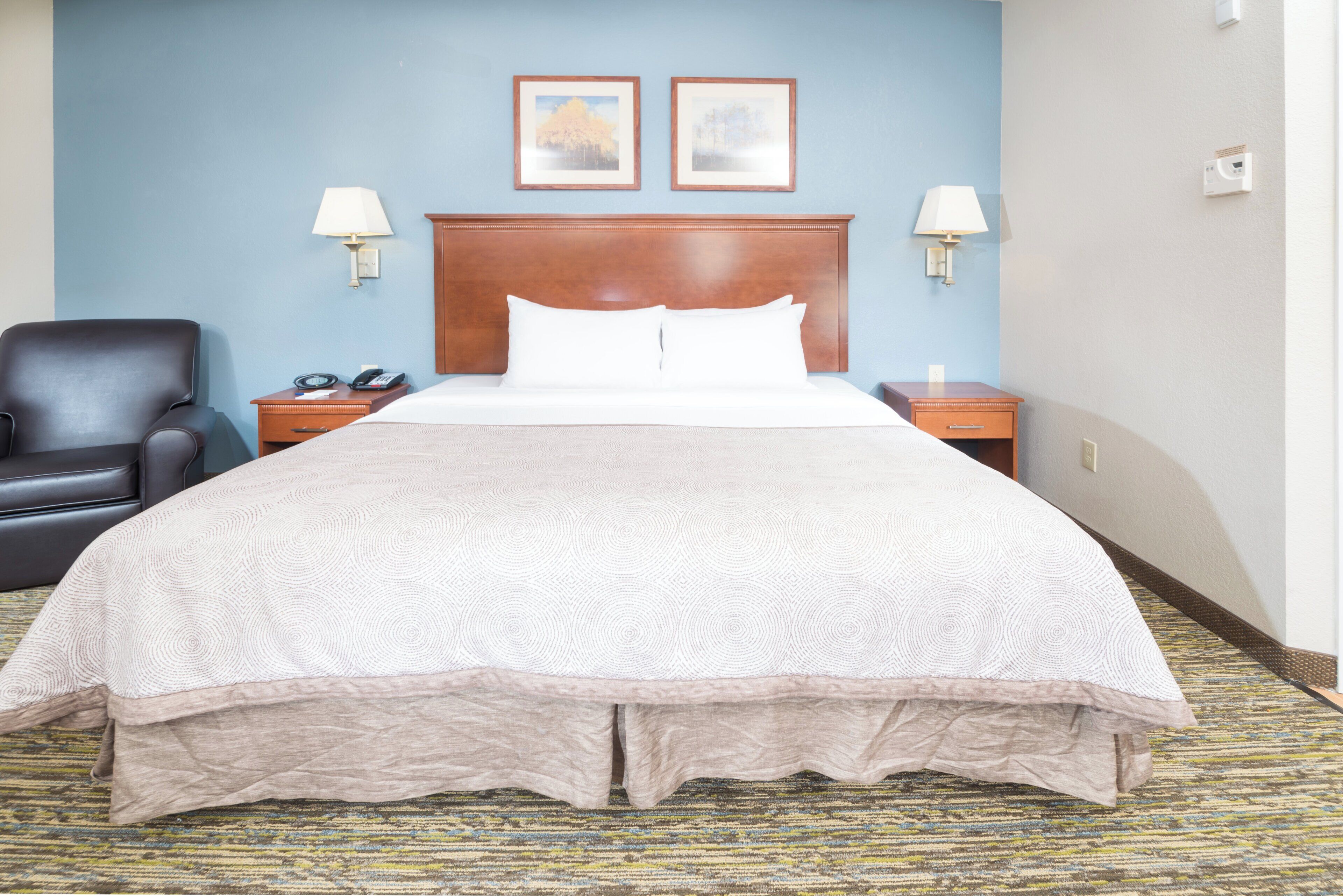 A hotel room with a large bed, a chair, a nightstand, two wall-mounted lamps, and two framed pictures on the wall.