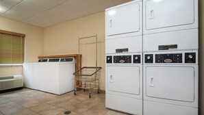 A laundry room with stacked washers and dryers, a metal laundry cart, and a vented dryer. - Candlewood Suites WAKE FOREST RALEIGH AREA by IHG (Wake Forest)