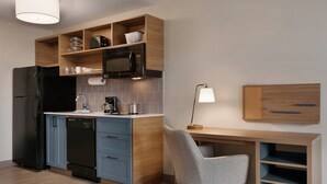 A modern kitchen with a built-in microwave, a refrigerator, and a dishwasher. There is a wooden desk with a chair and a lamp.