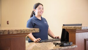 A person at a reception desk with a computer and a printer. - Candlewood Suites WAKE FOREST RALEIGH AREA by IHG (Wake Forest)