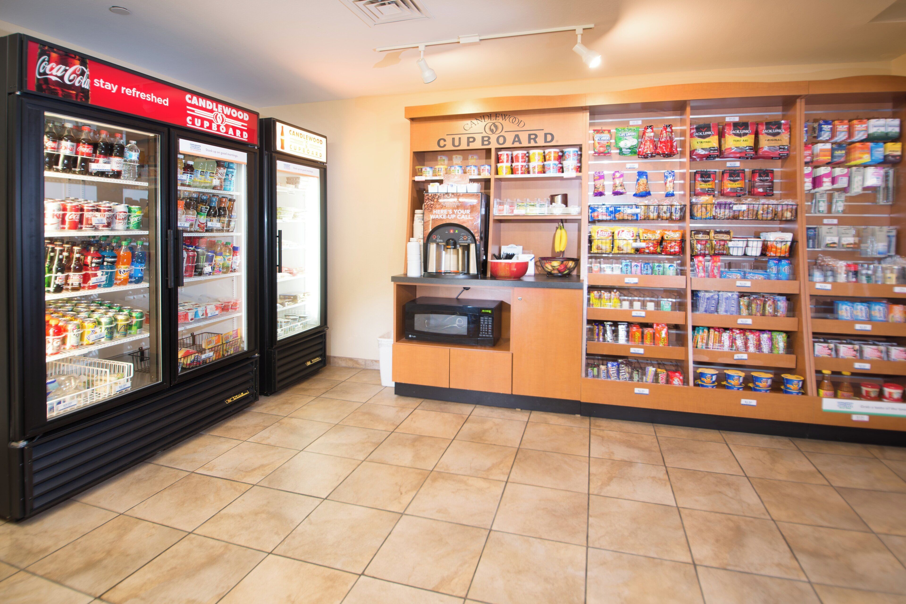 Una tienda de conveniencia con dispensadores de bebidas refrigeradas, un microondas y una variedad de snacks y bebidas en los estantes.