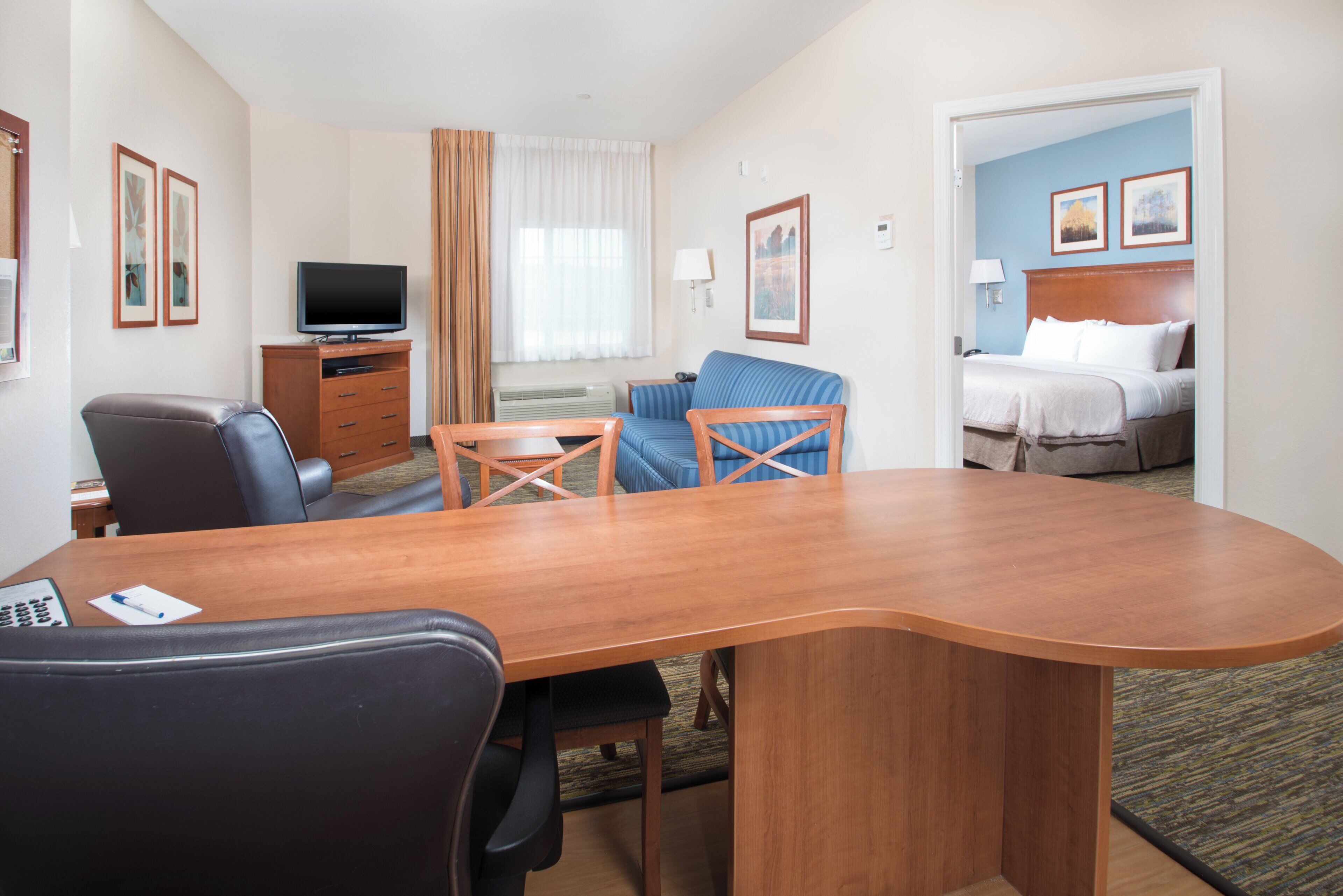 A hotel room with a wooden desk, two chairs, a television, a bed, and a bathroom.