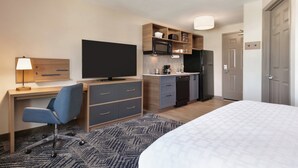 A hotel room with a bed, a desk with a chair, a television, a kitchenette, and a wardrobe.