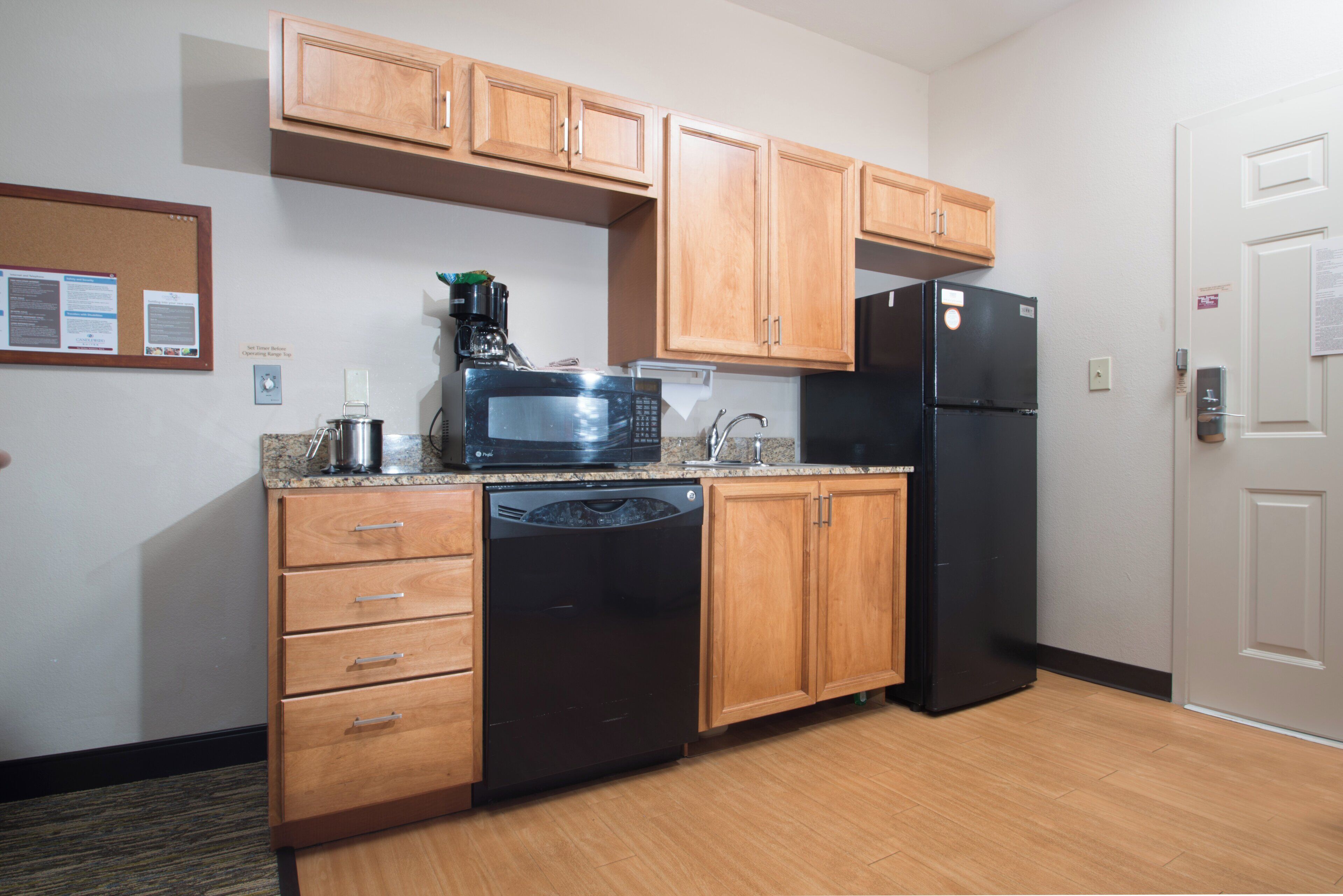 A compact kitchen with wooden cabinets, a black refrigerator, a microwave, a dishwasher, and a coffee maker.