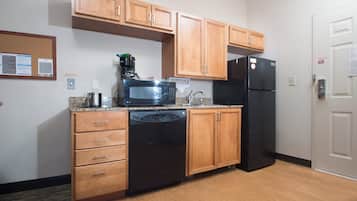 Cozinha compacta com armários de madeira, geladeira preta, micro-ondas, lava-louças e cafeteira.