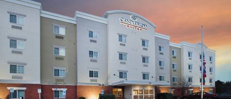 A multi-story hotel with a flat facade, a prominent hotel name sign, and a parking lot in front.