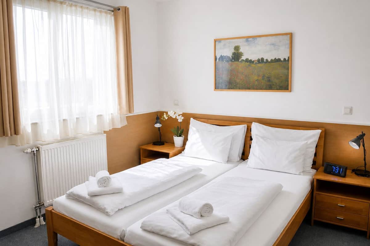 A hotel room with a double bed, two bedside tables, a night lamp, a potted plant, and a painting on the wall.