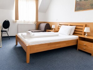 Una habitación de hotel con una cama de madera, una silla, un escritorio, una lámpara y un cuadro en la pared.