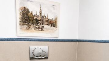 Un baño con inodoro, secador de manos, cubo de basura, dispensador de jabón para manos y soporte para papel higiénico.