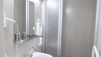 A bathroom with a sink, mirror, towel dispenser, and shower area.