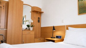 A hotel room with a bed, a nightstand with a clock, a dresser with a mirror, and a potted plant.