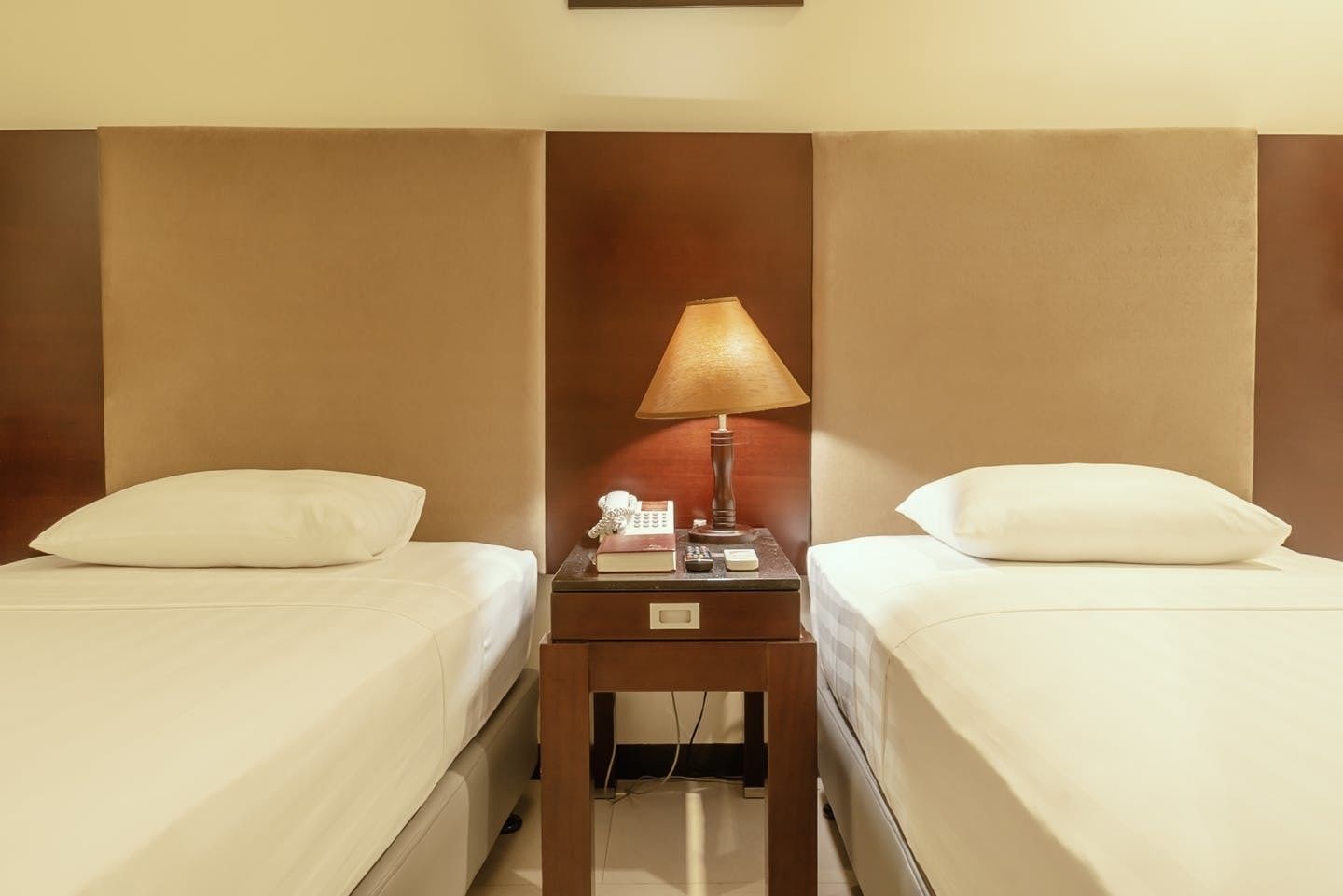 Une chambre d’hôtel avec deux lits simples, une table de chevet entre les deux, une lampe, un téléphone et un petit tiroir.
