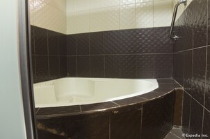 Un bagno con una vasca, pareti piastrellate scure e una zona doccia.
