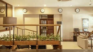 A modern hotel lobby with a wooden staircase, multiple clocks, a seating area, and a dining space. - Casa Bocobo Hotel (Manila)
