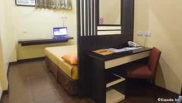 Habitación de hotel compacta con una cama individual, un escritorio con teléfono y un monitor de computadora.
