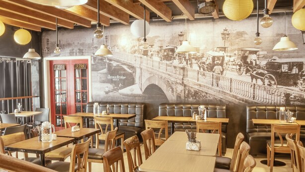 A restaurant with wooden tables and booths, a mural of a bridge, and hanging paper lanterns. - Casa Bocobo Hotel (Manila)