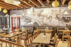 A restaurant with wooden tables and booths, a mural of a bridge, and hanging paper lanterns. - Casa Bocobo Hotel (Manila)