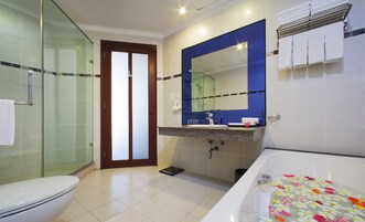 Un baño con cabina de ducha de vidrio, inodoro, lavabo con espejo y bañera con felpudos estampados de flores.