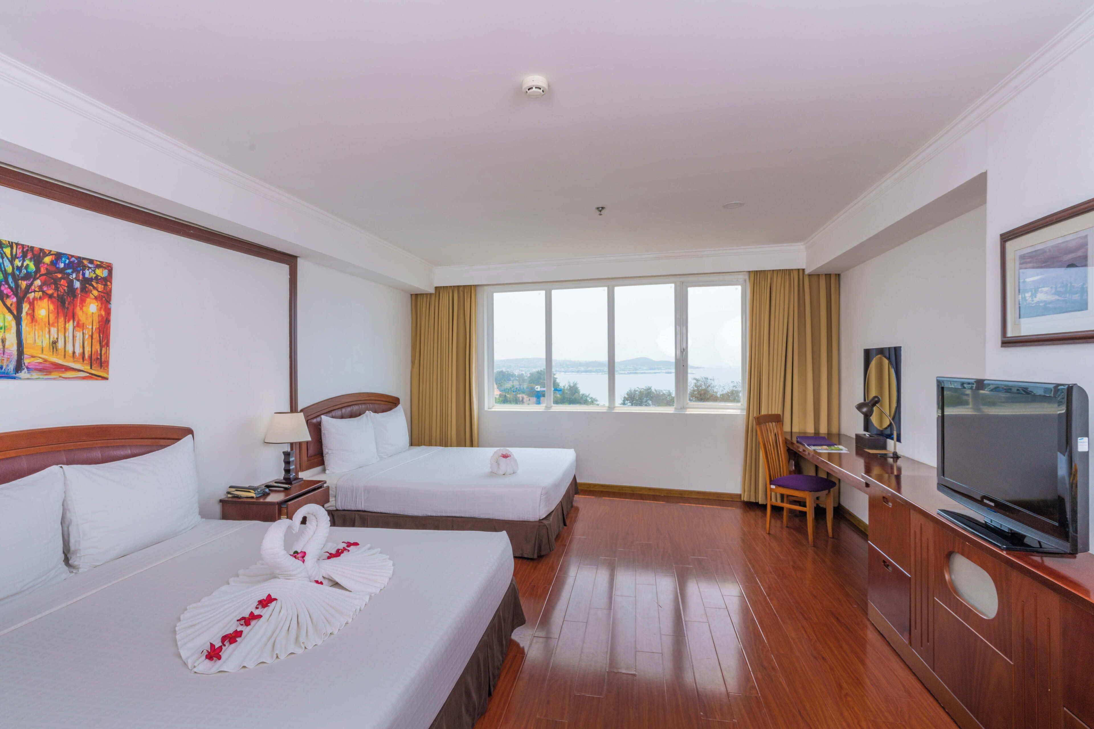 Habitación de hotel con dos camas, televisión, escritorio y ventana con vistas a la ciudad.