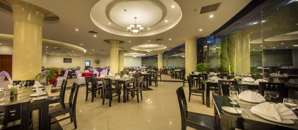 Un restaurant spacieux doté de nombreuses tables et chaises, de grandes colonnes et d’un plafond au design moderne, agrémenté d’un éclairage encastré.