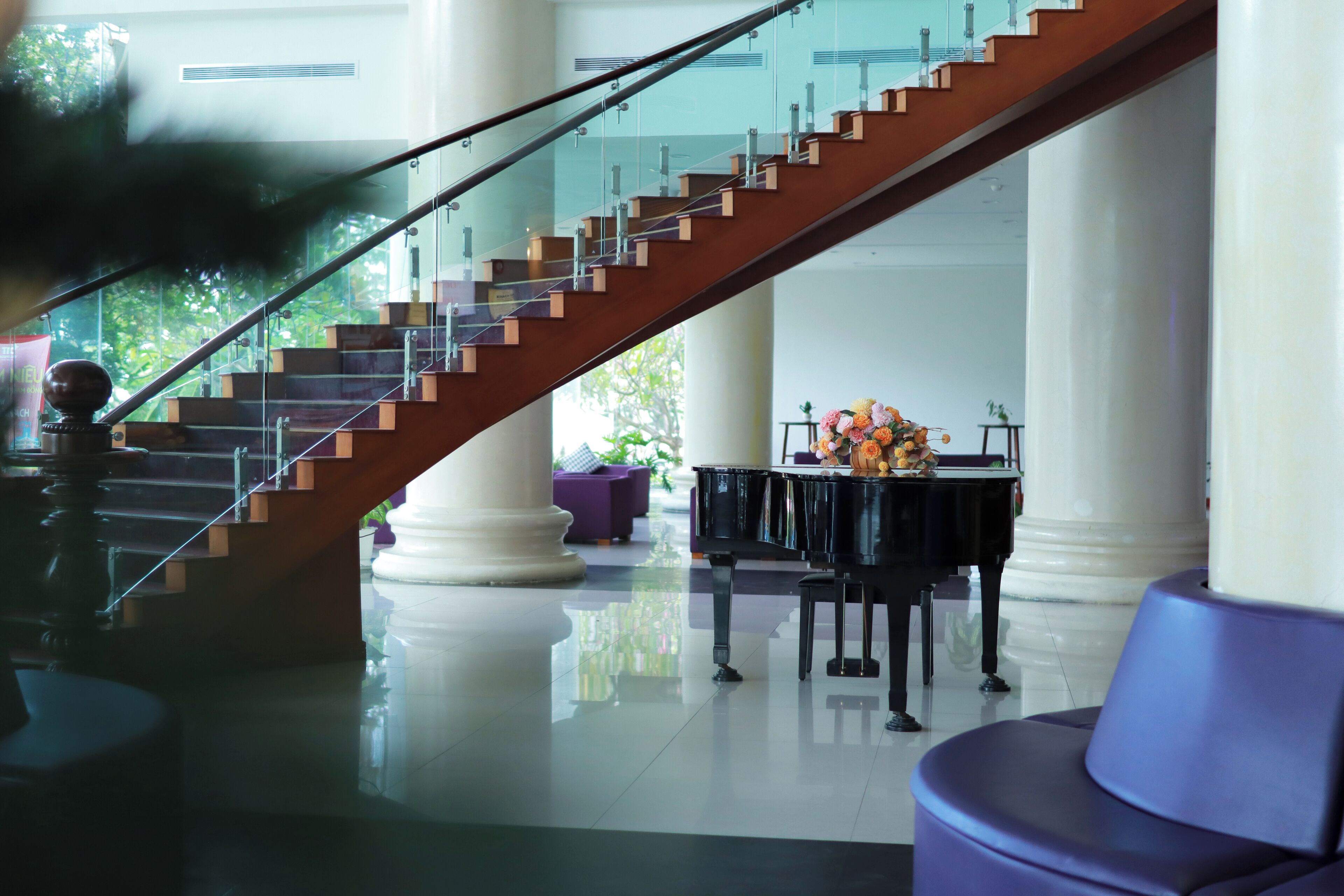 Una imponente escalera con barandillas de cristal, un piano y un área de descanso en un vestíbulo amplio.