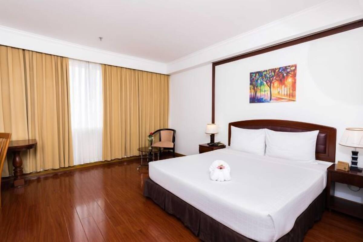 Une chambre d’hôtel avec un grand lit, un bureau, une chaise et un tableau au mur.