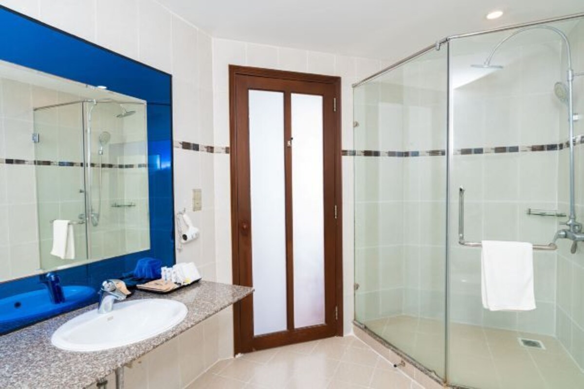 A bathroom with a glass-enclosed shower, a sink with a blue-tiled vanity, and a large mirror.