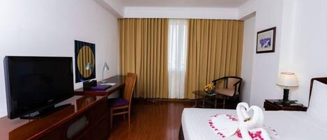 A hotel room with a bed, a TV, a desk, a chair, and a window with curtains.
