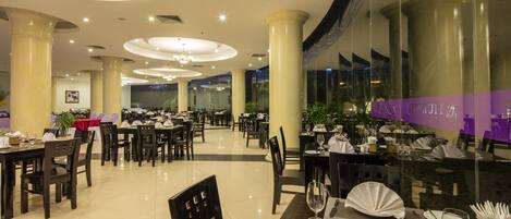 Un vaste espace dédié à la salle à manger, avec de nombreuses tables et chaises, de grandes colonnes et un lustre moderne.