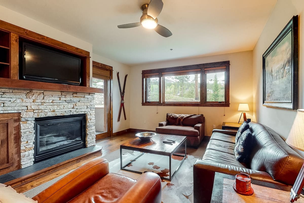 A living room with a stone fireplace, leather sofa, and a flat-screen TV mounted above it.
