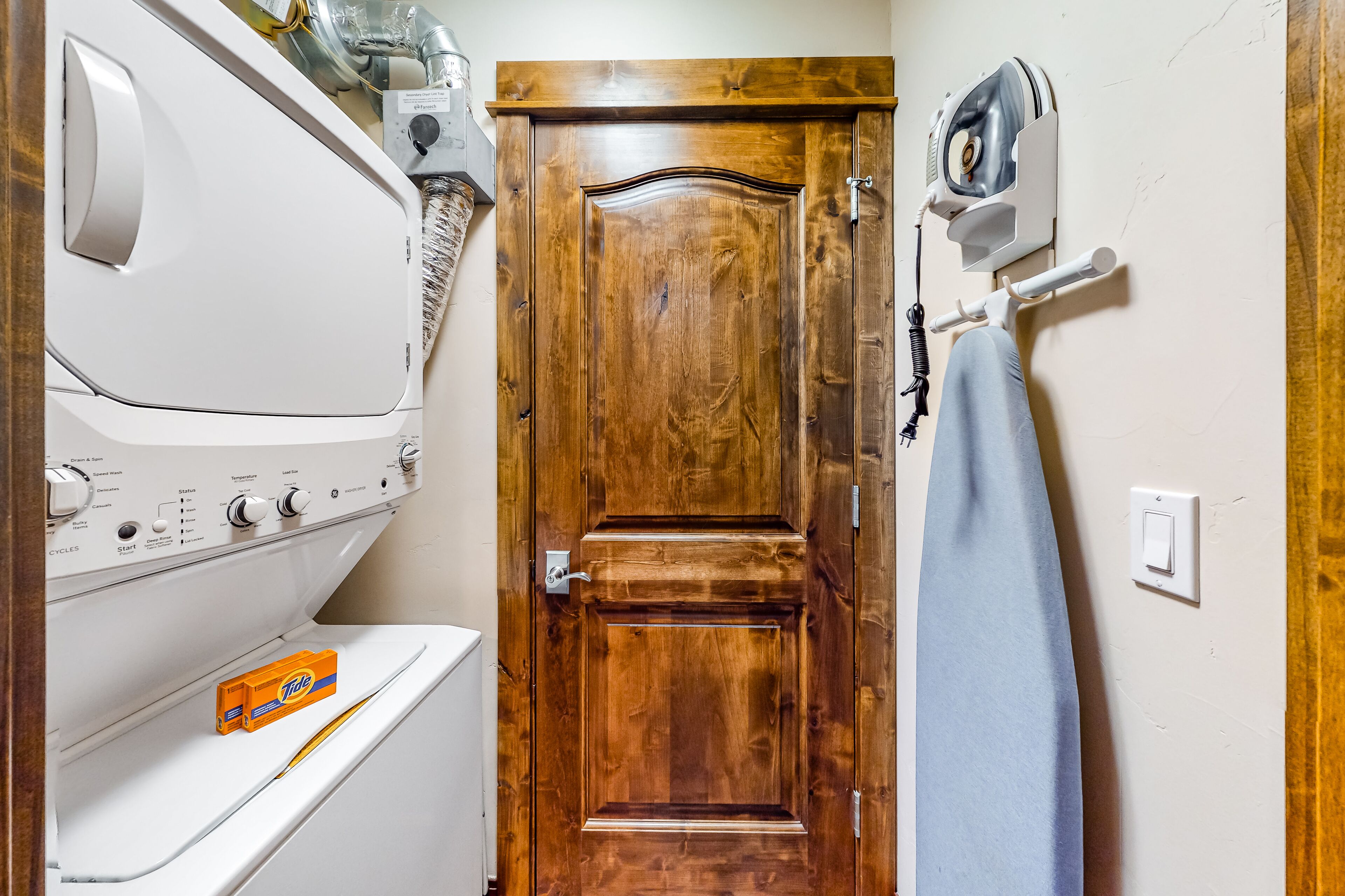 A laundry room with a white dryer, a wooden door, and a wall-mounted iron.