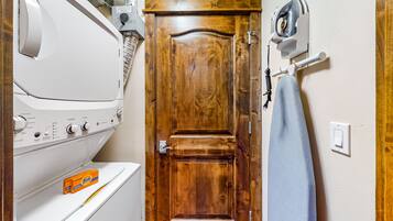 Un lavadero con una secadora blanca, una puerta de madera y una plancha fijada a la pared.