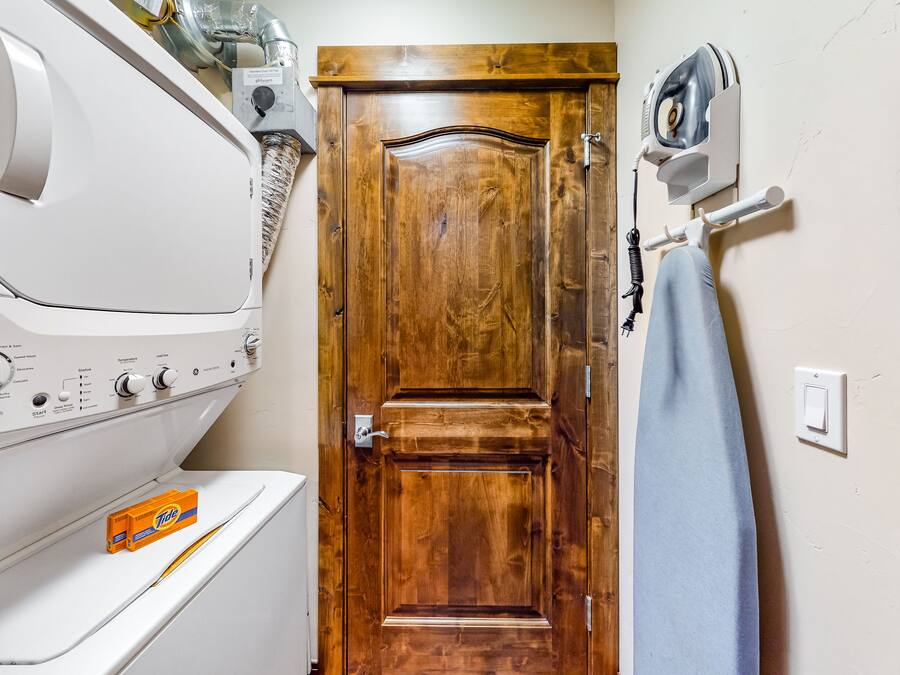 Un lavadero con una secadora blanca, una puerta de madera y una plancha fijada a la pared.