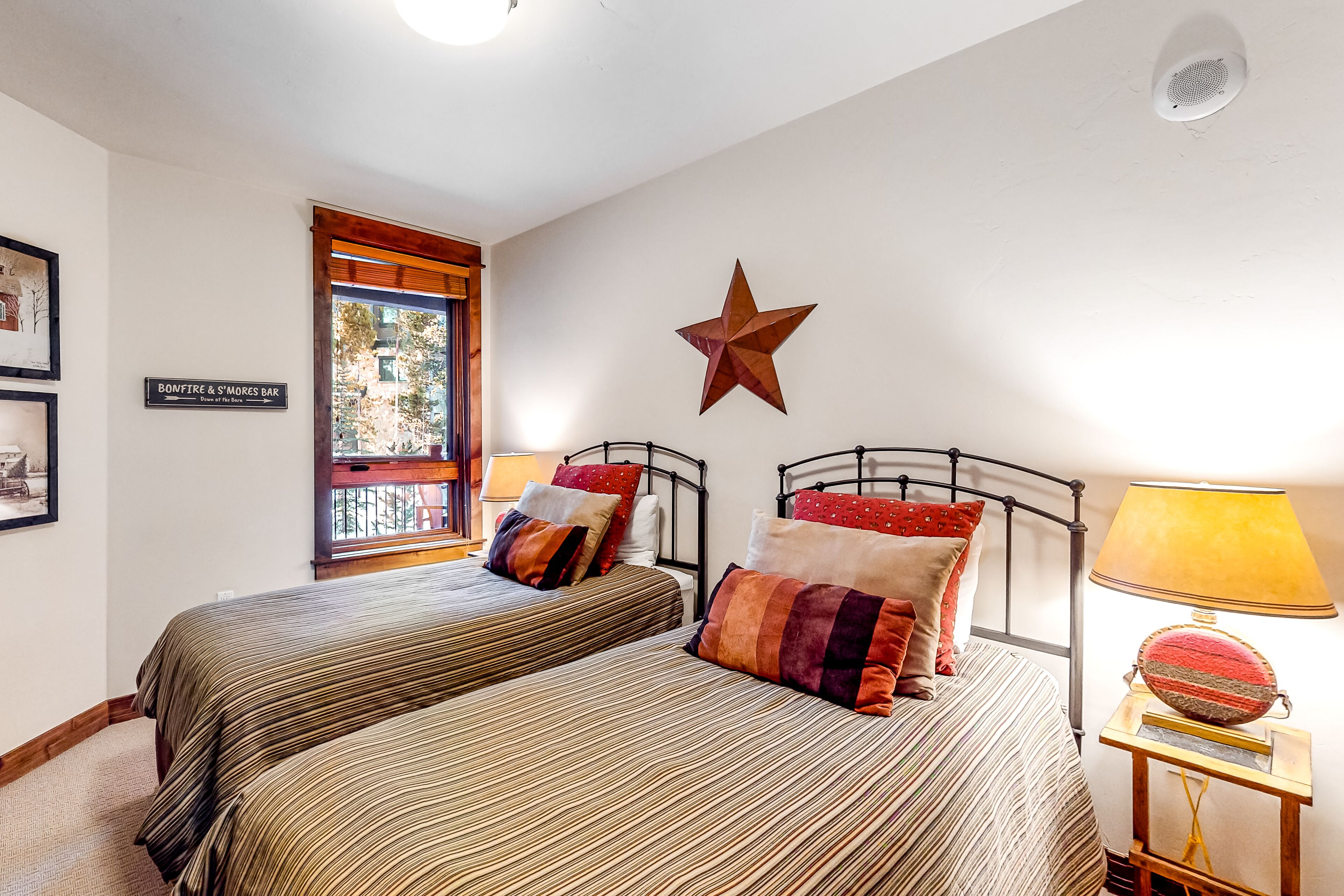 A bedroom with two beds, a star decoration, a window with a view, and a sign for Bonfire & S'mores Bar.